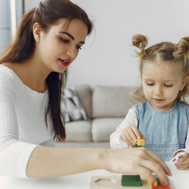 Woman in White Long Sleeve Shirt Playing with a Girl in Denim Dress