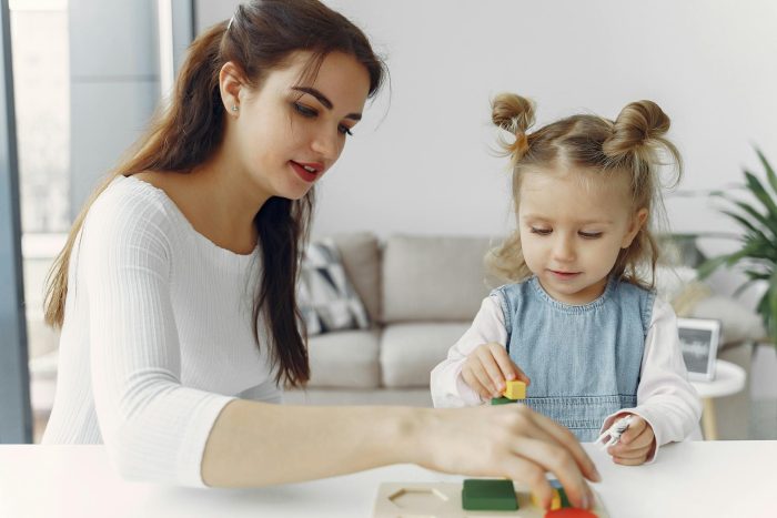 Woman in White Long Sleeve Shirt Playing with a Girl in Denim Dress